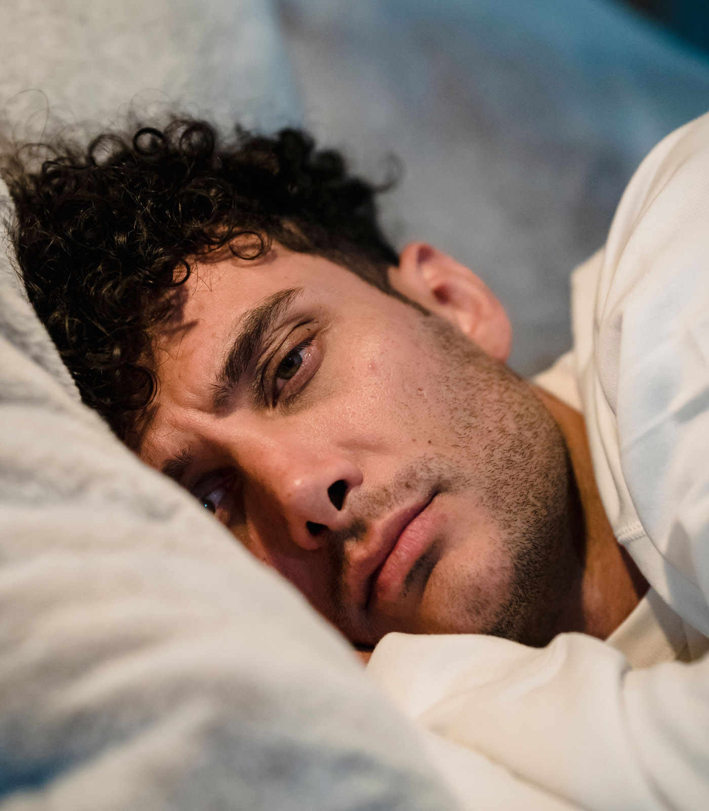 A man lying awake in bed, looking tired and restless